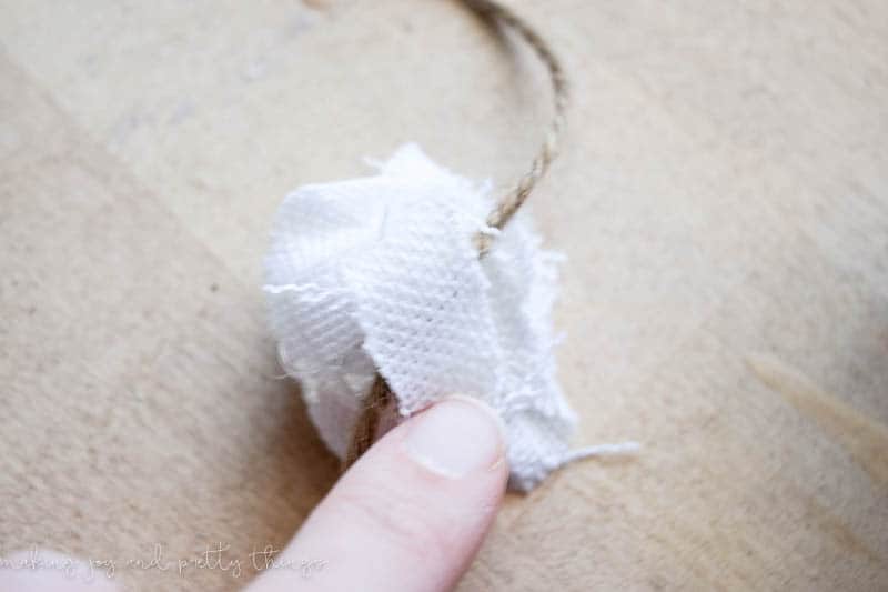 attaching a no sew fabric flower to twin with hot glue and fabric to make a long and farmhouse style garland