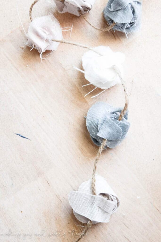 DIY fabric flowers strung along a line of twine to make a no sew farmhouse style garland with rustic accents