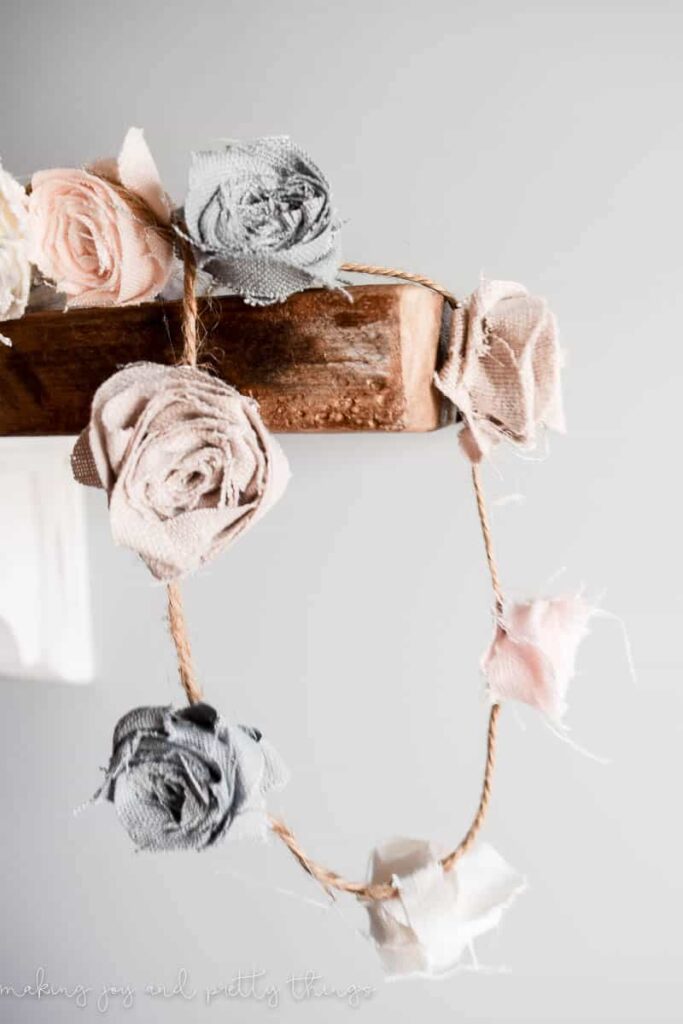 DIY fabric flowers strung into a garland with hot glue and a no sew technique hung on rustic shelves in a nursery