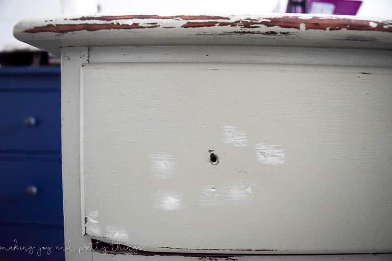 A close up image of the top drawer of an old thrifted dresser. The drawer handle has been removed and there's white spackle covering some gauges in the drawer surface. The dresser has been sanded down, revealing some of the natural wood color underneath.