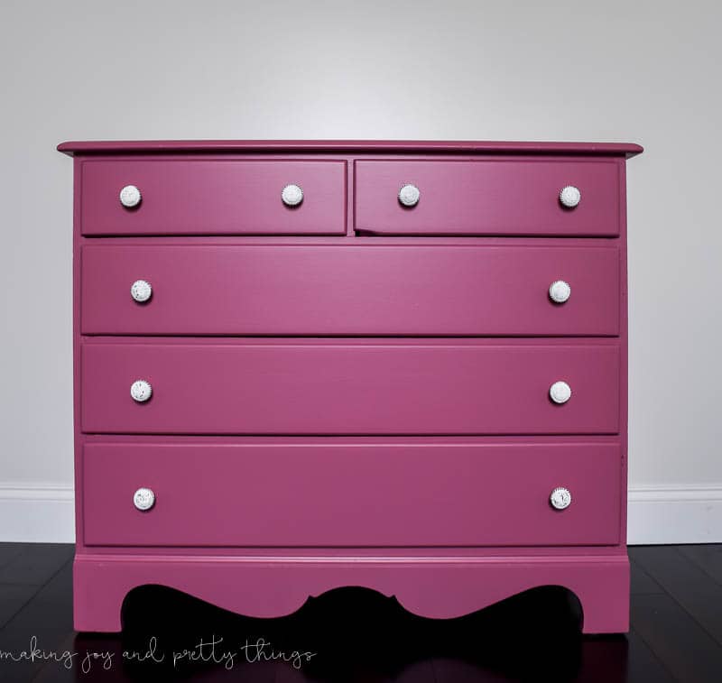 A complete look at the finished DIY pink dresser makeover! The five-drawer dresser is painted a dark mauve pink color, and each drawer has new white round knob handles.