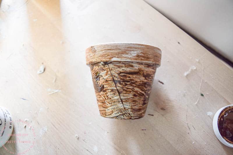 A decoupaged terracotta pot covered with brown antique wax sits on a wood table.