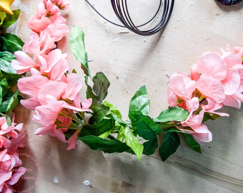 DIY flower wreath using fake flowers that are pink in a circle attached with floral wire