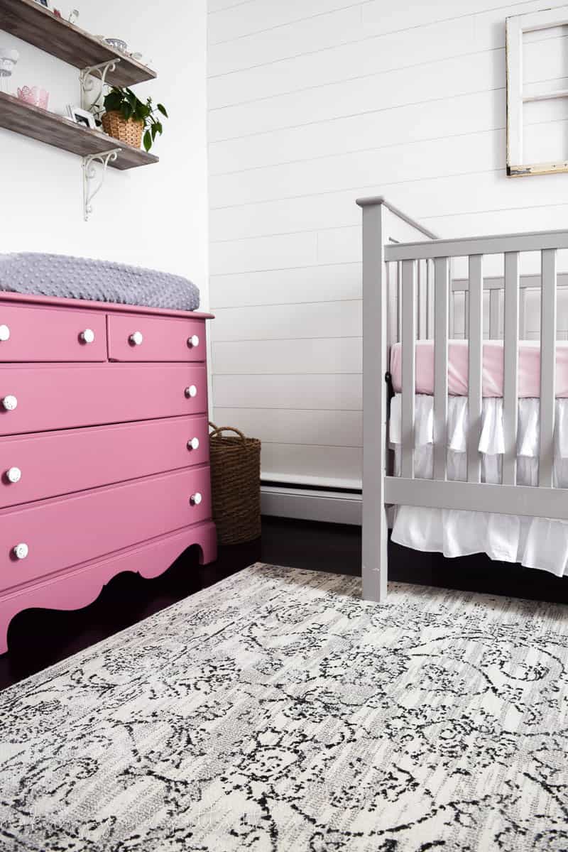 The nursery changing table - and upcycled dresser painted pink, the crib, and area run in our baby girl's farmhouse style nursery.