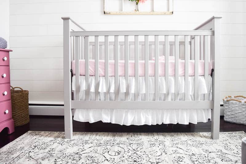 Cozy crib in a farmhouse nursery over a floral rug that sets the tone for a room and is a great piece of decor 