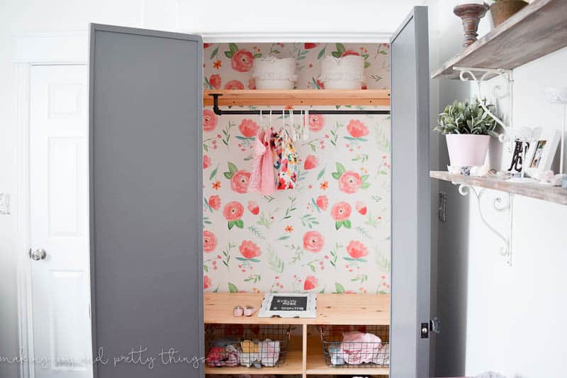 Open closet that has a wallpaper accent with custom shelves and baskets to store farmhouse nursery clothes and decor