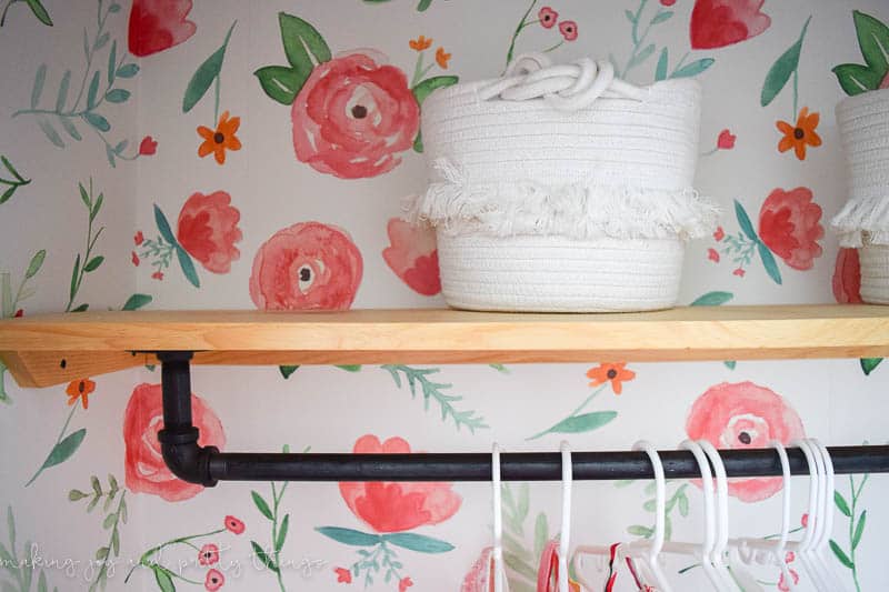Closet shelf made in a custom style with black iron pipe and wood decorated with baskets in a nursery 
