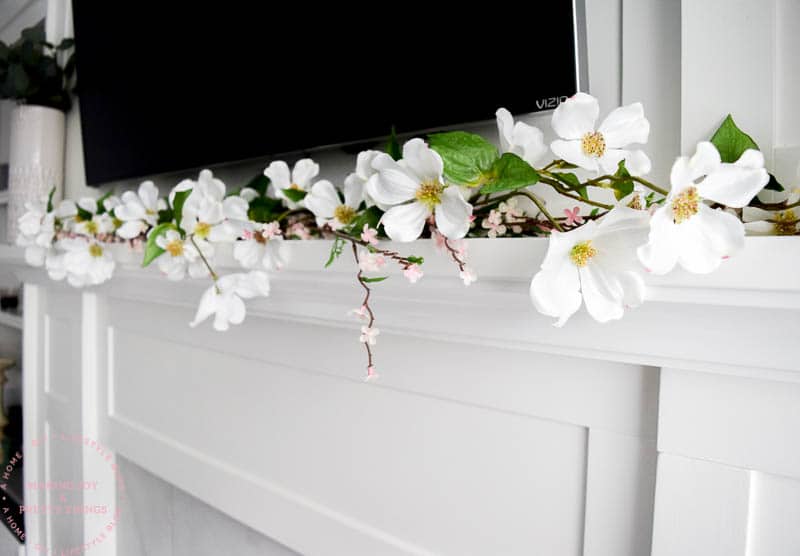 A farmhouse fireplace mantel decor with tv with magnolia flowers and spring blossoms made into a garland