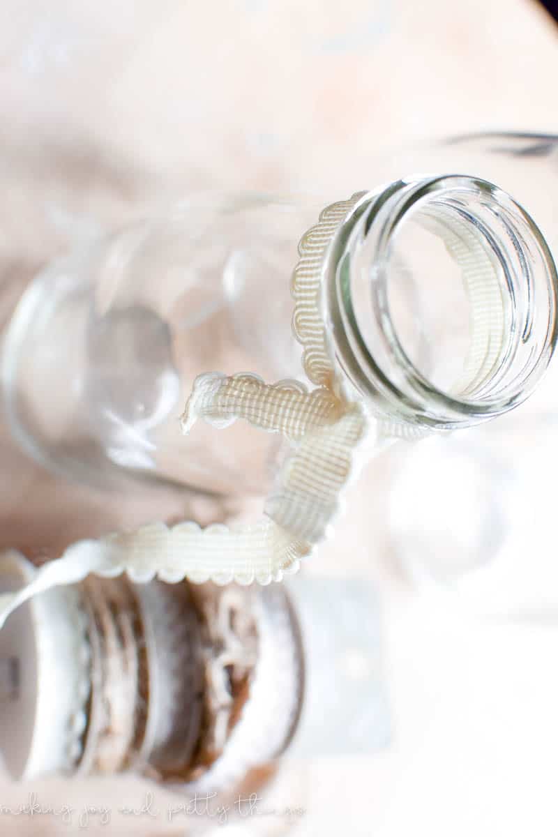 Using ribbon to decorate the top of a milk jar to make a decoration that hangs with flowers inside