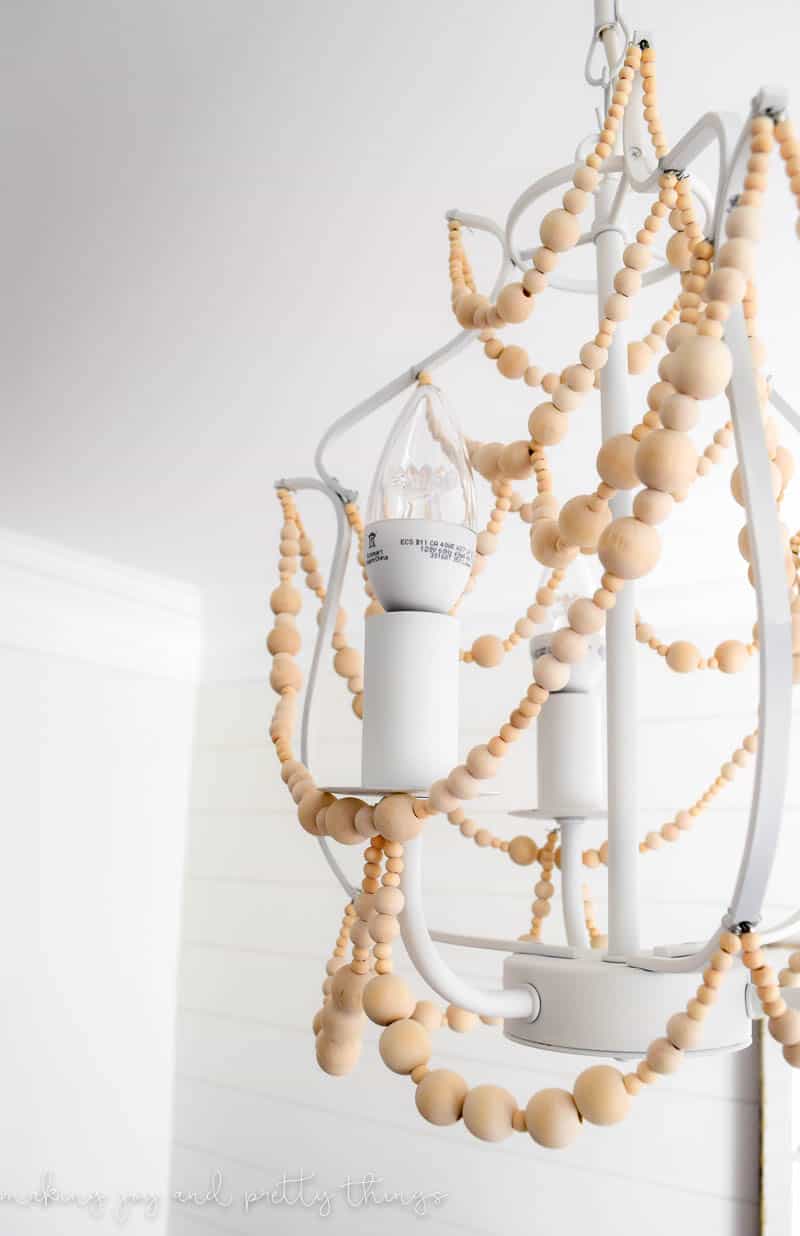 A closeup look at the strands of wood beads hanging from a white-painted chandelier body.