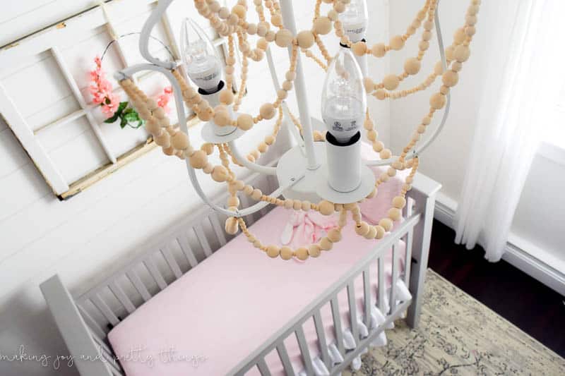 A view of the DIY wood bead chandelier looking down over the baby's crib - rows of wood beads hang from a white framed chandelier.