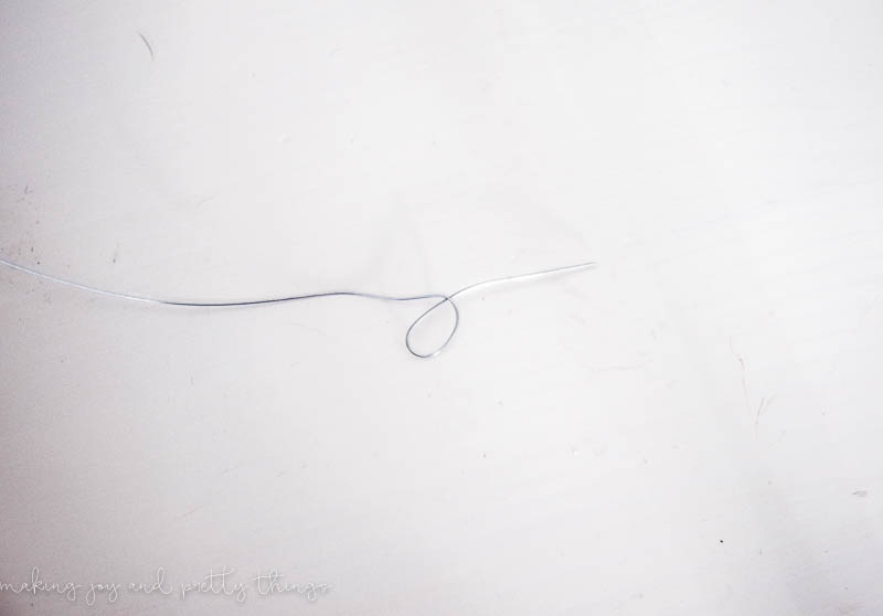 A thin strand of wire, with a loop twisted at the end, ready to be beaded for the diy wood bead chandelier.