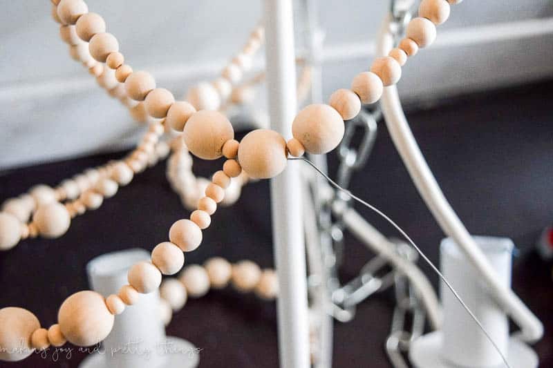 Sections of wood beads hang from the chandelier, with a length of wire poking out.