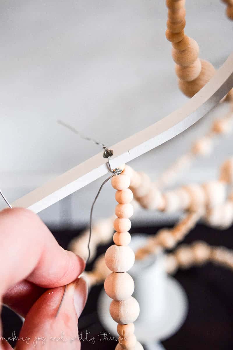 A close up look at how to thread the strands of wood beads onto the chandelier body, and anchor them using wire.