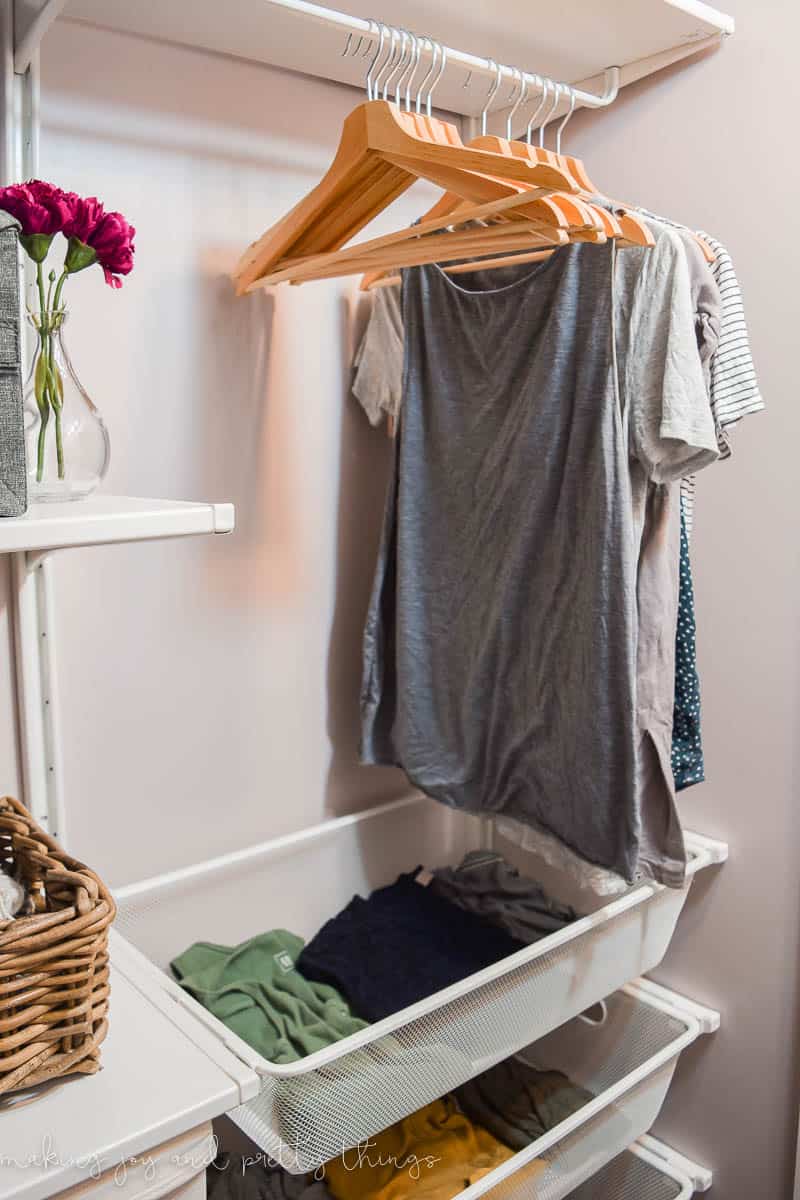 A closer look at the cloth hanging rods attached to the wall-mounted shelving in our walk-in closet. Shirts hang on wooden clothes hangers.