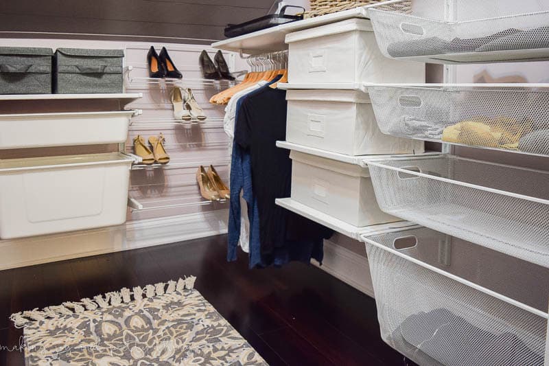 Another look at the closet storage system, featuring wall-mounted shelving that holds storage bins and baskets for easy clothes storage, clothes hanger rods for hanging clothing, and a wall-mounted she rack.
