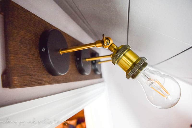 A side view of the industrial farmhouse style light fixture installed in our walk-in closet. The fixture sits above the door, close to the slanted ceiling and features three industrial style light fixtures with clear bulbs.