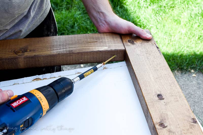 Using a drill to add screws on an inside angle to sturdy up a frame for an exterior frame 