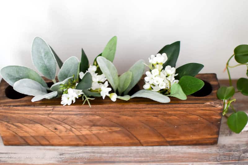 Farmhouse style sugar mold sitting on floating shelf holding faux flowers 