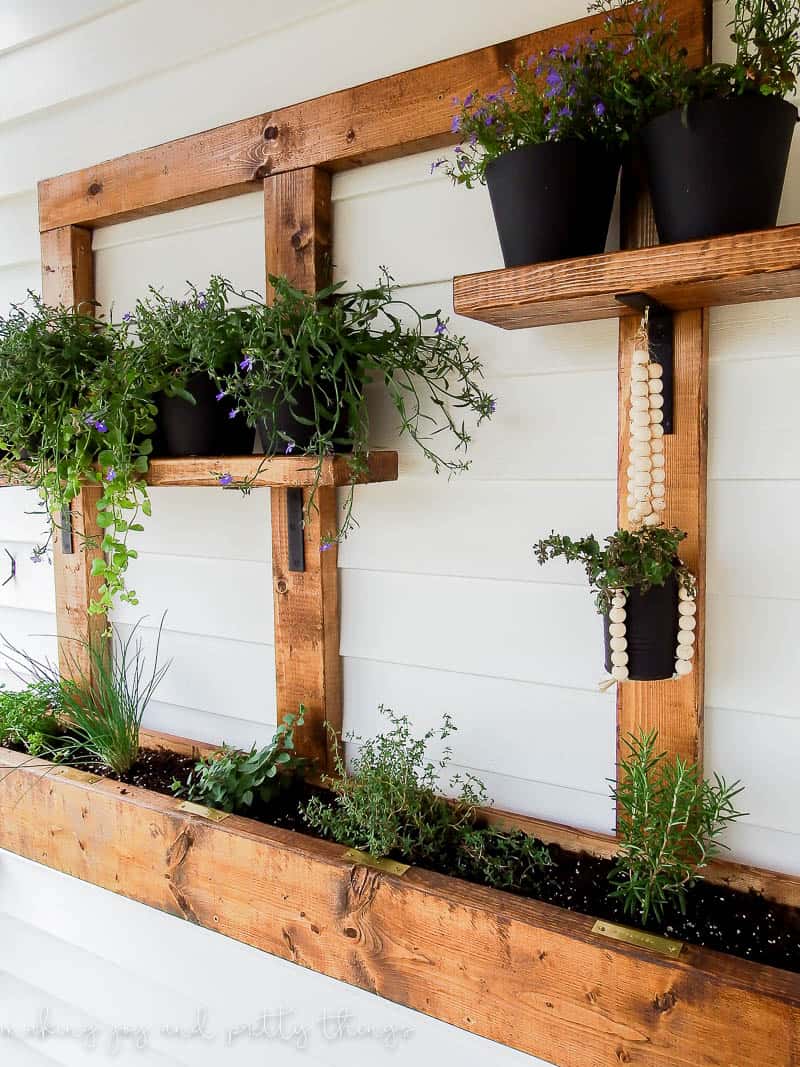Revealing a DIY vertical herb garden and planter box with shelves and stained wood that is hung up outside