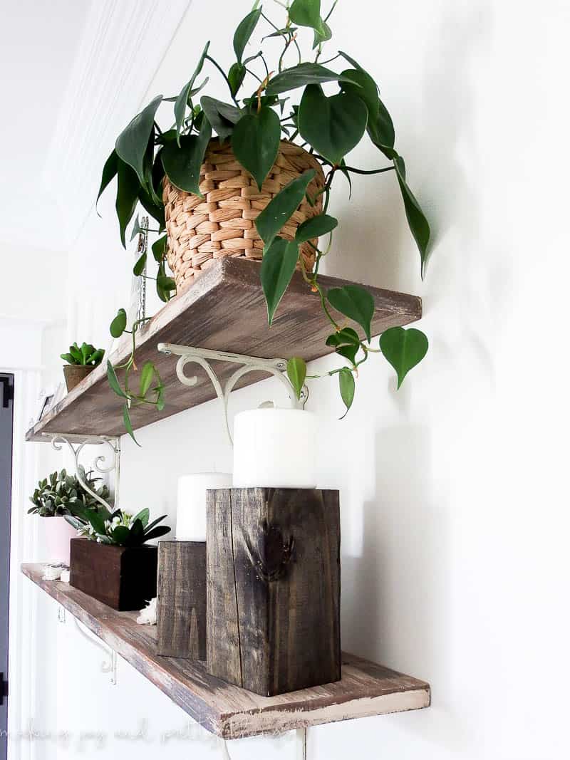 Floating shelves made with barn wood and metal brackets in bedroom decorated with plants and candles