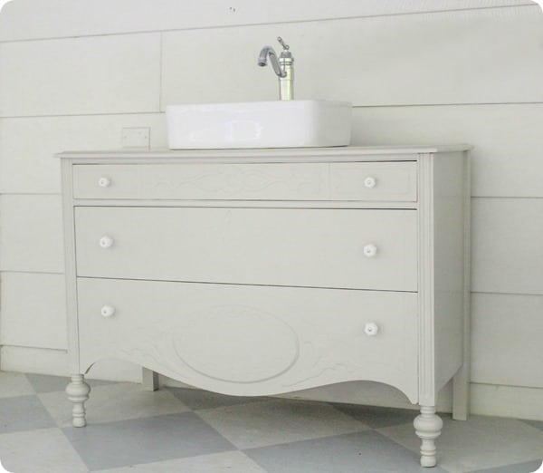 A modern dresser painted white to serve as a vanities in a bathroom remodel with a white sink.
