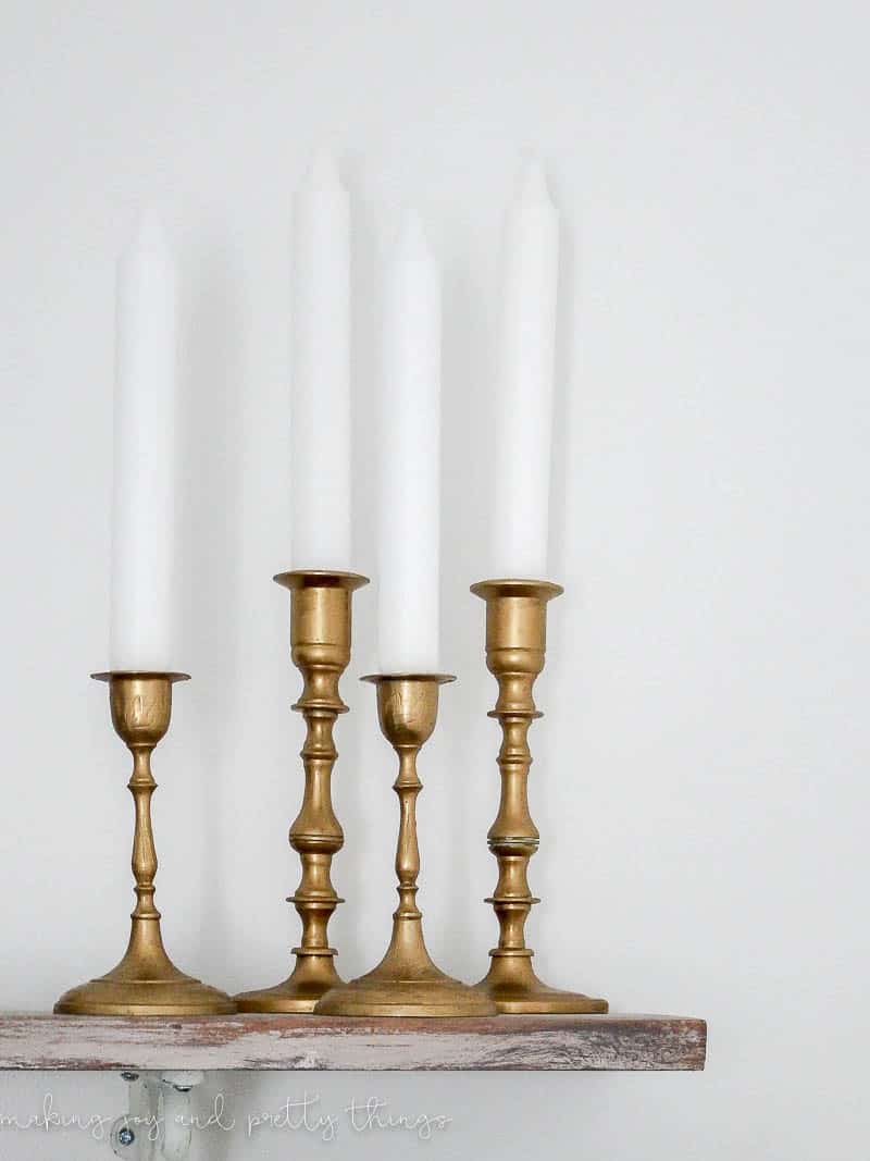 A set of four thrift store candleholders with white pillar candles. Learn how we gave these old candleholders a stunning gold finish with an easy candleholder makeover.