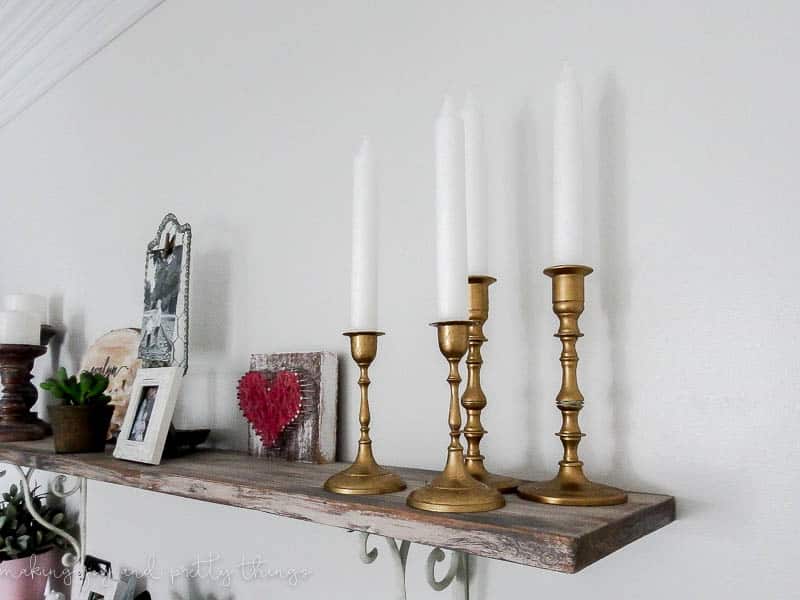 This set of four thrift store candleholders sit on a farmhouse style floating wood shelf, along with other farmhouse style decor. Learn how we gave them a shiny golf finish with this candleholder makeover!
