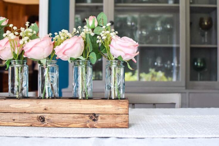 See how I used a scrap 2x4 board and transformed it into a simple wooden farmhouse style centerpiece using 5 blue glass vases.  Add in some beautiful silk roses and you have a gorgeous, easy centerpiece!
