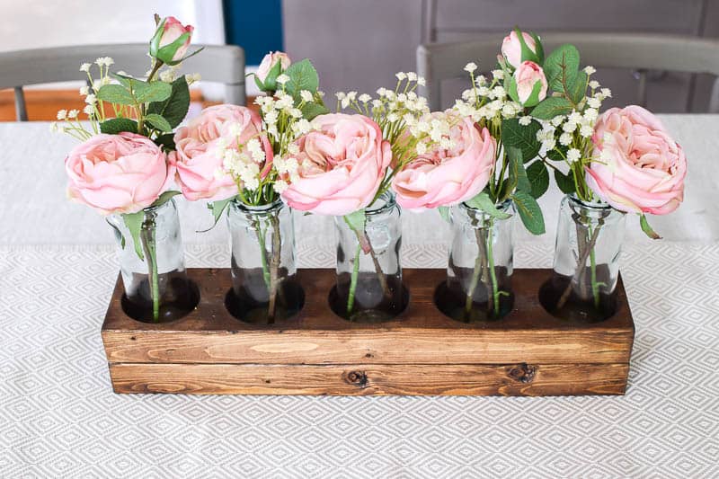 Using glass bottles and flowers with greenery to are great ideas to give a farmhouse look to your dining room table