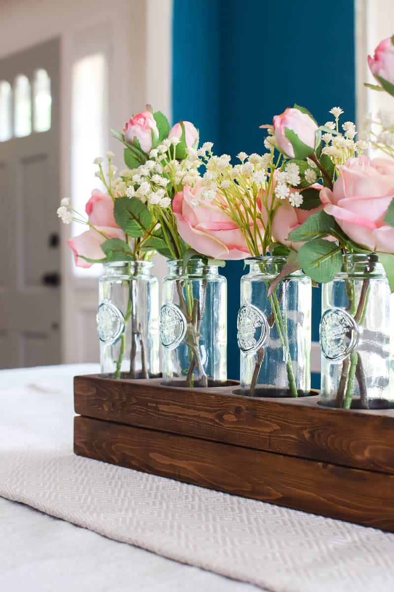 See how I used a scrap 2x4 board and transformed it into a simple wooden farmhouse style centerpiece using 5 blue glass vases.  Add in some beautiful silk roses and you have a gorgeous, easy centerpiece!