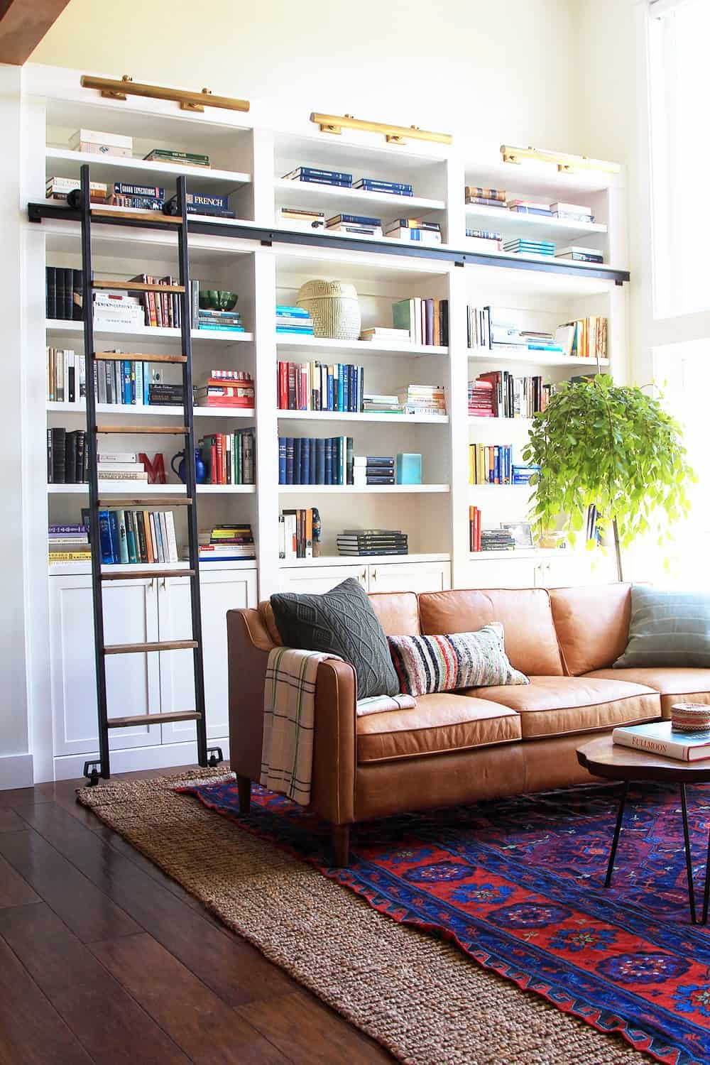 A living space with a cabinet stocked full of books and an intricate leather couch with layered rugs on the floor showing a colorful vintage rug put on top of a jute rug