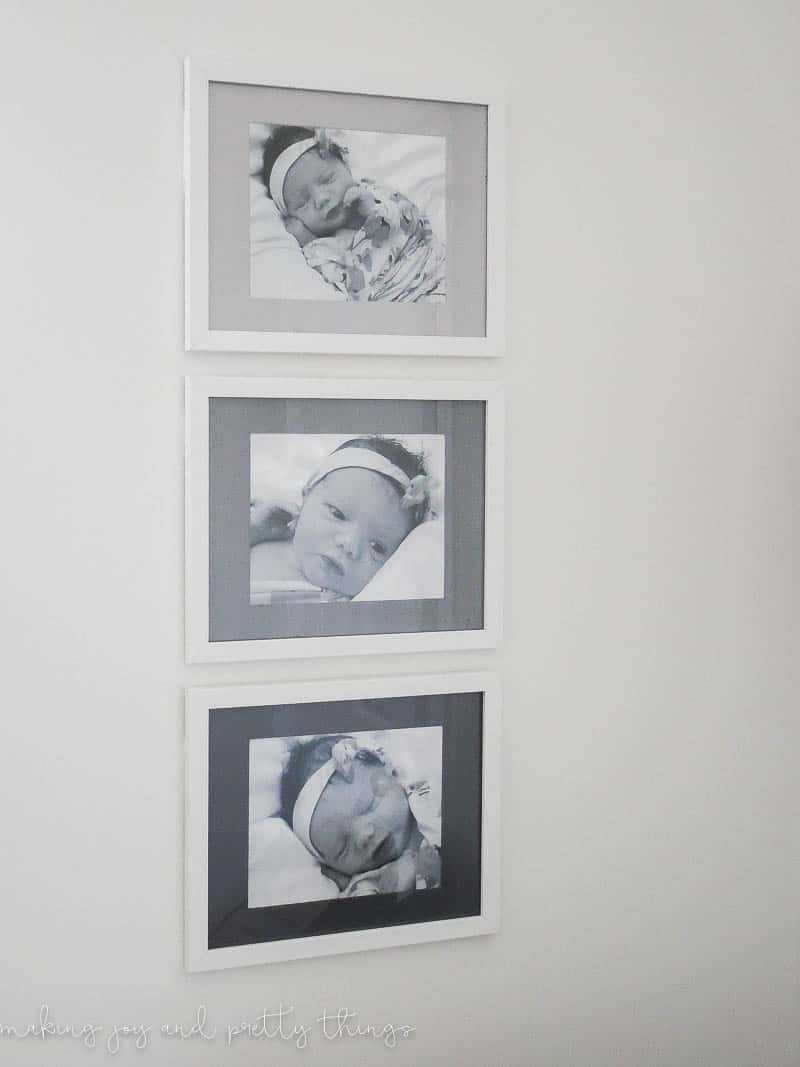 A closer look at the three ombre picture frames hanging on a white wall. The white-framed pictures each hold a back and white photo of a newborn baby. The frame mats are painted light grey, medium grey, and black.