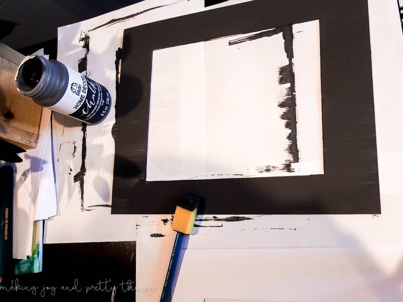 An image showing the process of painting mat boards with a dark, almost black, chalk paint.