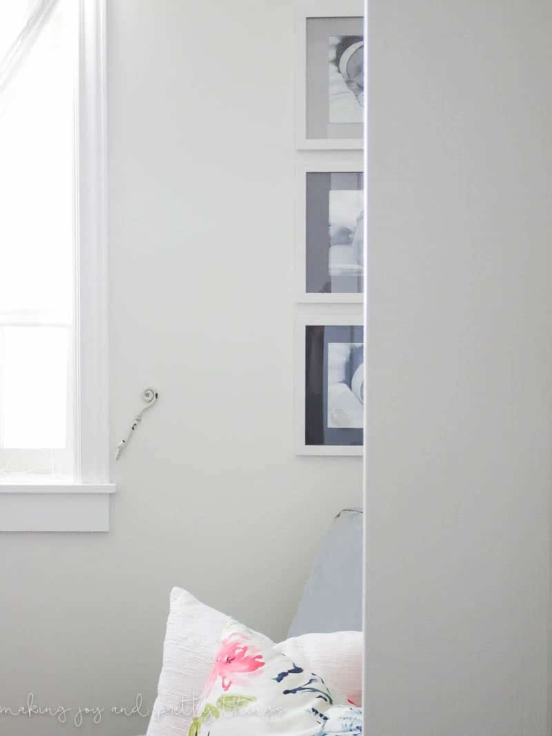 Three white-framed baby pictures with painted mat boards hang on a wall, half obscured by a wall. The mat boards within the photo frames are painted black, gray, and a lighter gray, creating an ombre effect. 