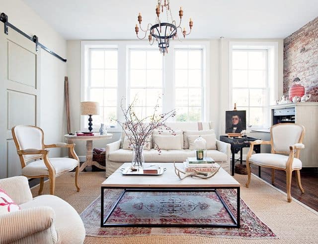 A bright living room area with a large square coffee table surrounded by arm chairs and a couch. The room is filled with natural light and bright, contemporary decor.