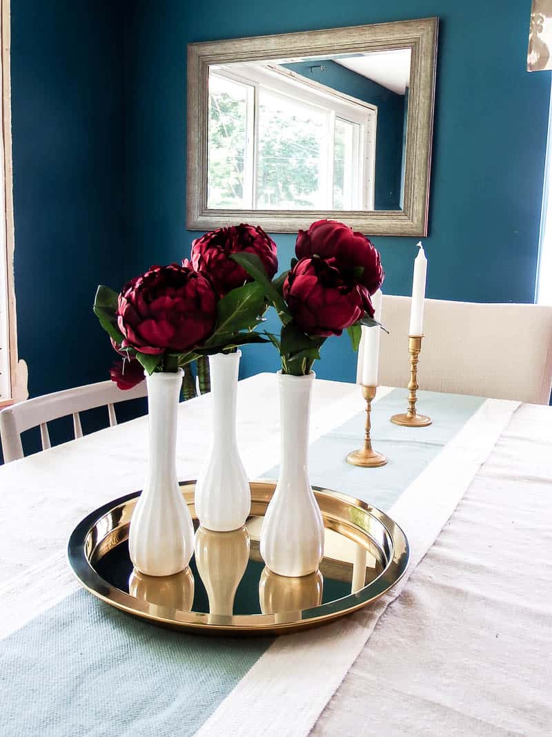 Faux floral arrangement on a gold plated dish with dark red flowers and greener used as a table decoration