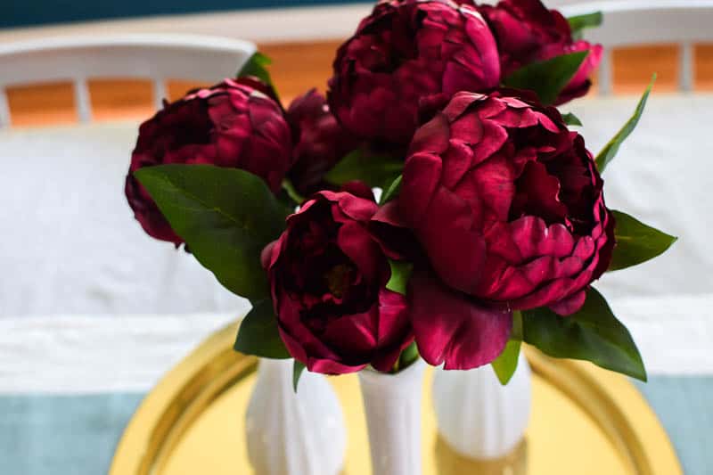Deep rich burgundy flowers put in thrift store vases on a gold dish to make a beautiful flower arrangement for a table