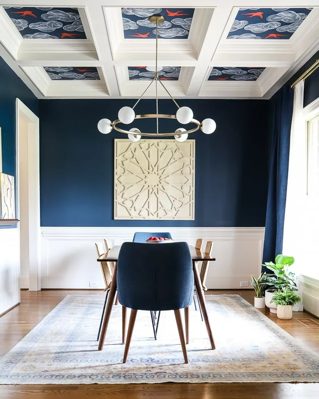 Dark navy blue dining room with white painted wainscoting on the lower part of the walls with a ornate tray ceiling with wallpaper incorporated into the ceiling