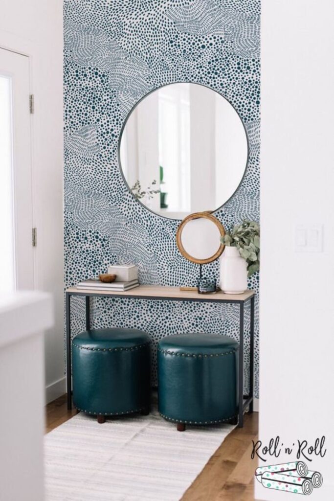 Dalmatian spot patterned wallpaper with blue color scheme in hanging in an entryway behind a console table with a round mirror on the wall
