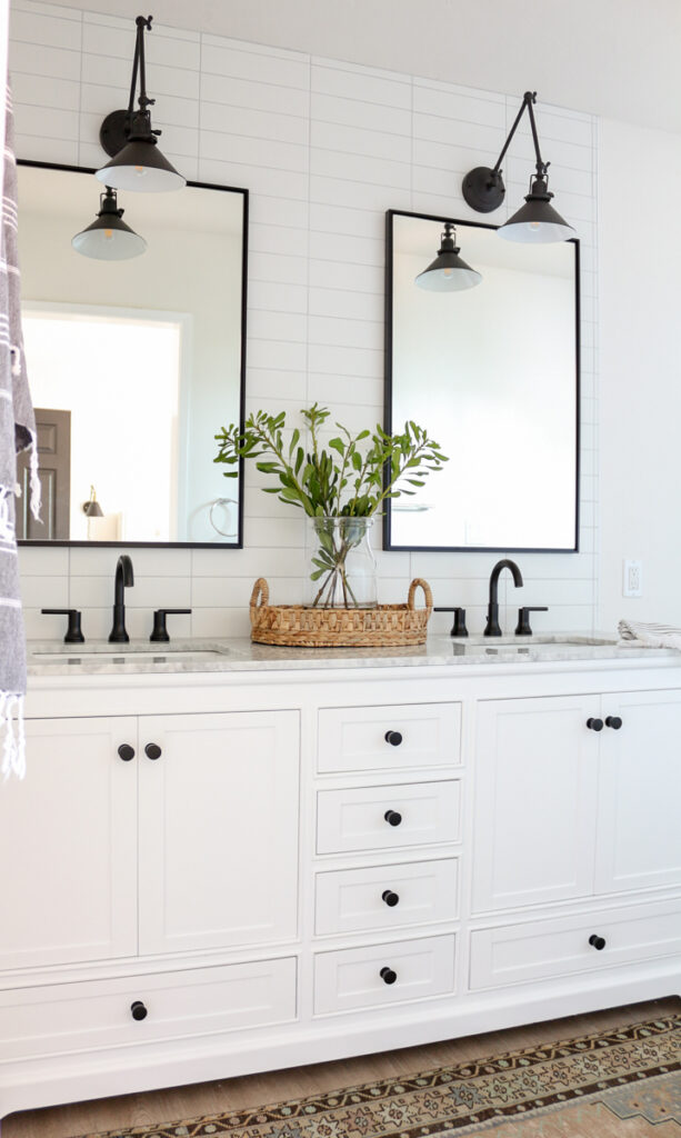 This modern farmhouse bathroom is black and white, with white subway tiled walls accented with light grout. The white double vanity has black hardware, and the metal-framed black mirrors provide contrast on white accent tiled wall.