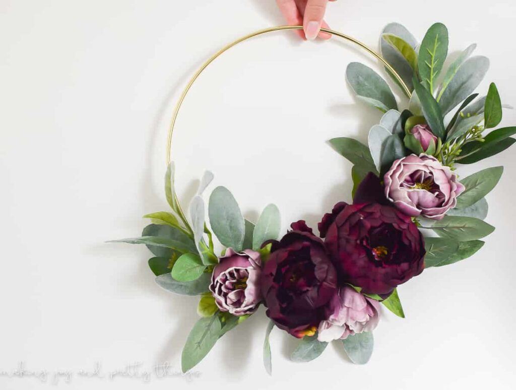 A floral wreath made with a gold hoop, faux flowers in rich jewel tones - a deep wine red and ombre purple - and eucalyptus leaves.