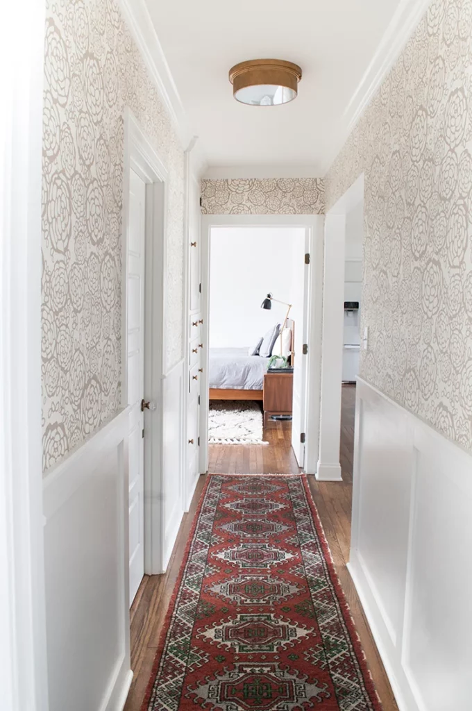 Hallway with gold and cream wallpaper installed above the white wainscoting.