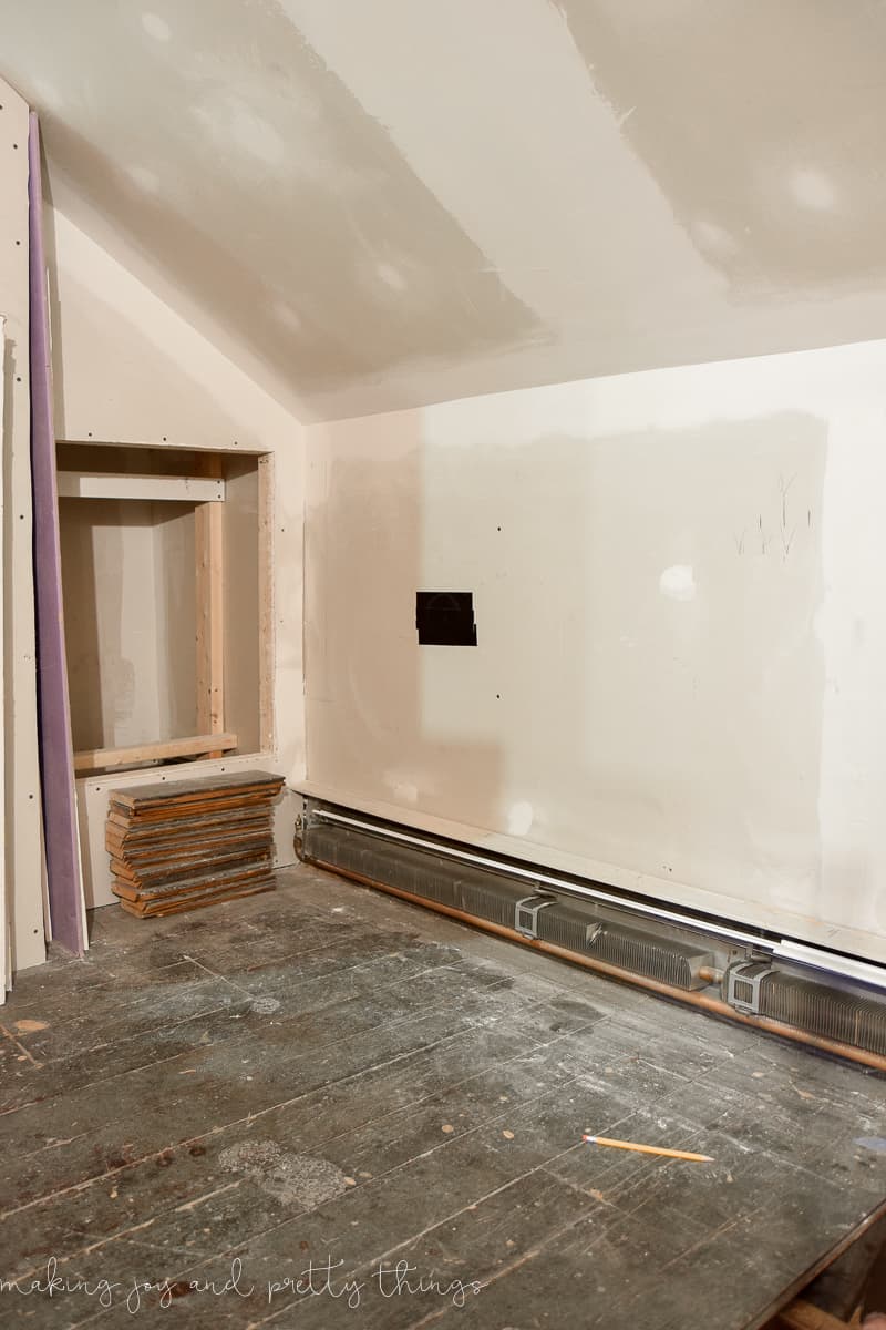 Our master bathroom mid-renovation - a gutted out room with exposed dry wall, paneled wood flooring, and stacked wooden boards.