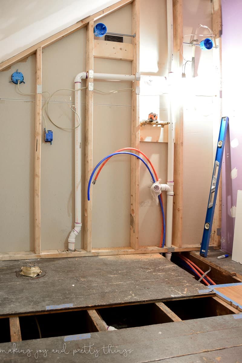 An exposed wall showing plumbing and other improvements made in a closet using a modern bathroom mood board as inspiration