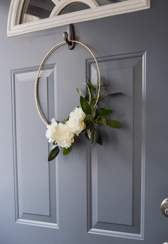 A DIY winter wreath with a gold ring white flowers and beautiful greenery hung on the front door after Christmas