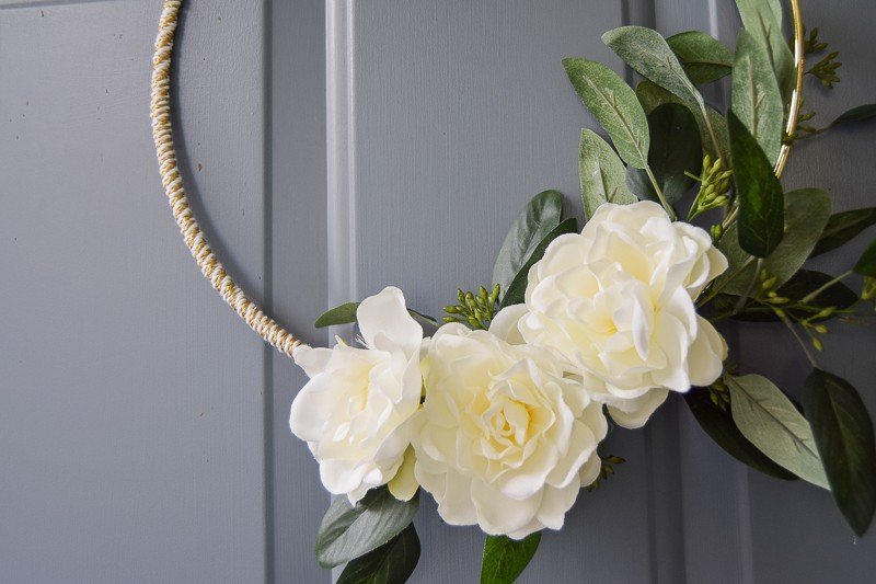 White flowers glued to a gold macrame ring to make a front door decoration with greenery 
