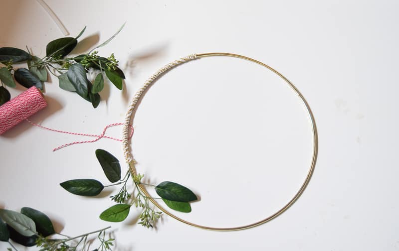 Attaching greenery to the DIY winter wreath with hot glue and wrapping the stem with twin to secure
