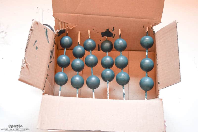 Using sticks and a carboard box to paint wooden beads to use for a garland is clean and simple