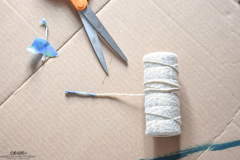 Tape one end of the gold and white twine to keep the frayed ends down to be used for threading large beads together